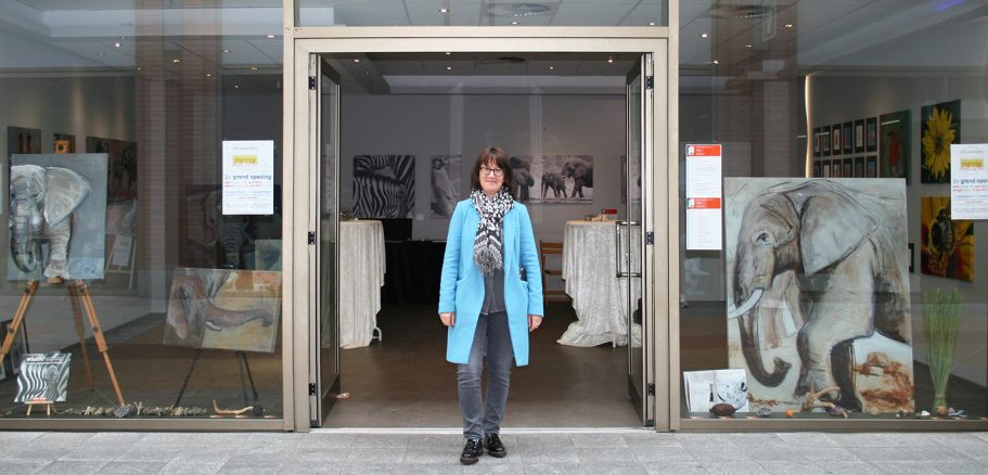 Frau mit blauer Jacke vor einem Kunstgalerie-Eingang mit Bildern.