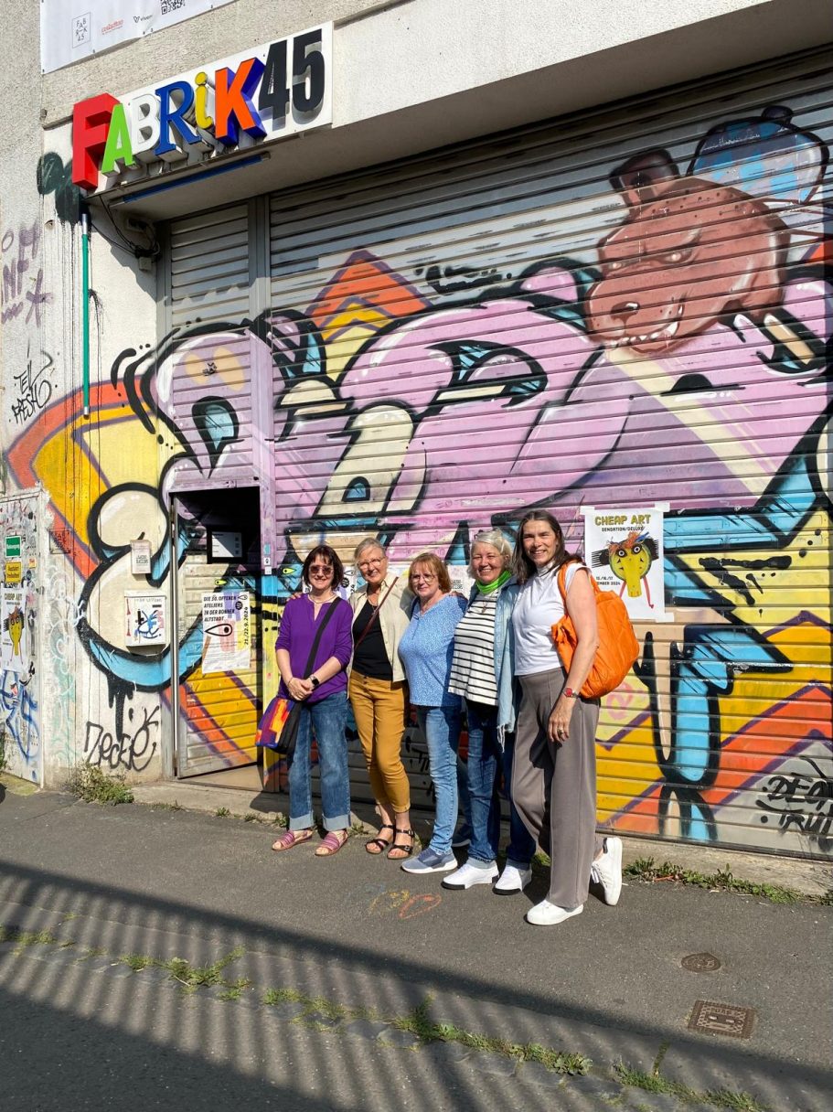 Gruppentreffen vor einer bunten Graffiti-Wand an einem Fabrikgebäude.