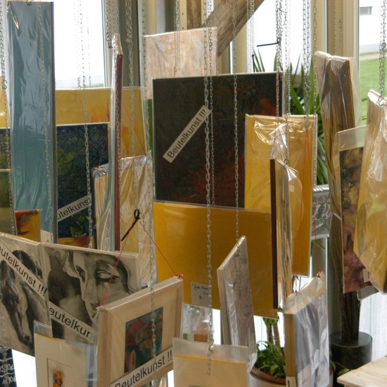 Verschiedene Kunstwerke in durchsichtigen Hüllen, auf Regalen präsentiert.