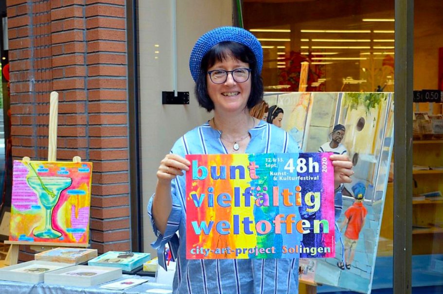 Frau mit blauer Mütze hält ein buntes Plakat mit der Aufschrift „bunt vielfältig weltoffen“.