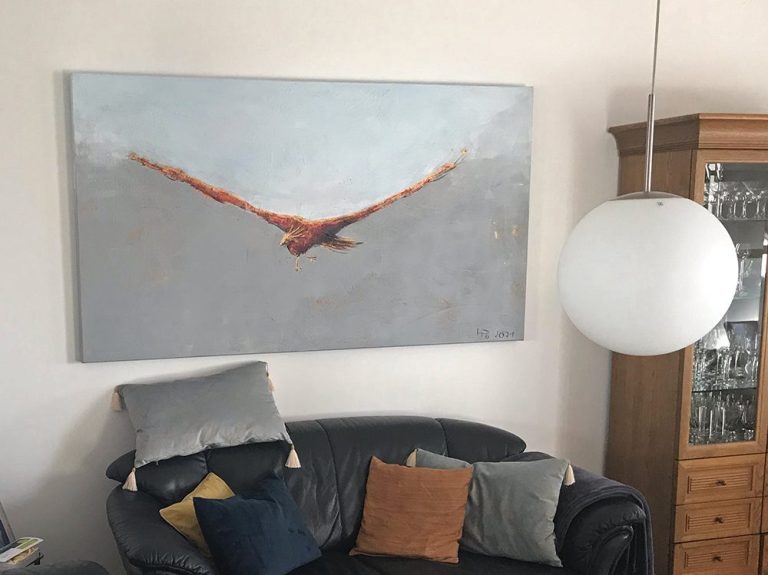 Ein Gemälde eines Vogels im Flug über einem Wohnzimmersofa mit Kissen.