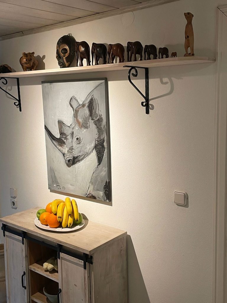 Eine Wand mit einem Rhinozeros-Bild und einer Regalreihe mit Tierfiguren. Darunter steht ein Obstkorb.