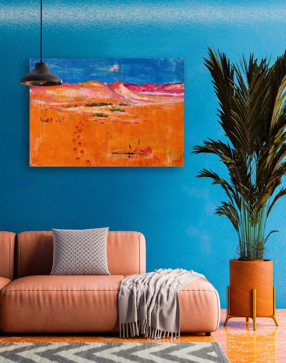 Heike Ponge Art | Spuren in der Wüste Namib mit Oryx | 100x70cm Abstraktes Gemälde in warmen Farben an einer blauen Wand, über einem beigen Sofa mit Kissen.