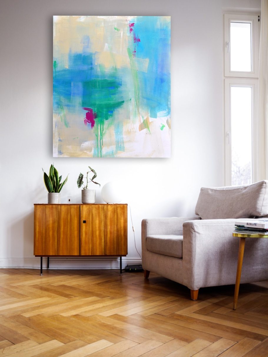Moderne Einrichtung mit beigem Sessel, Holztisch, Pflanze und farbenfrohem Kunstwerk an der Wand.