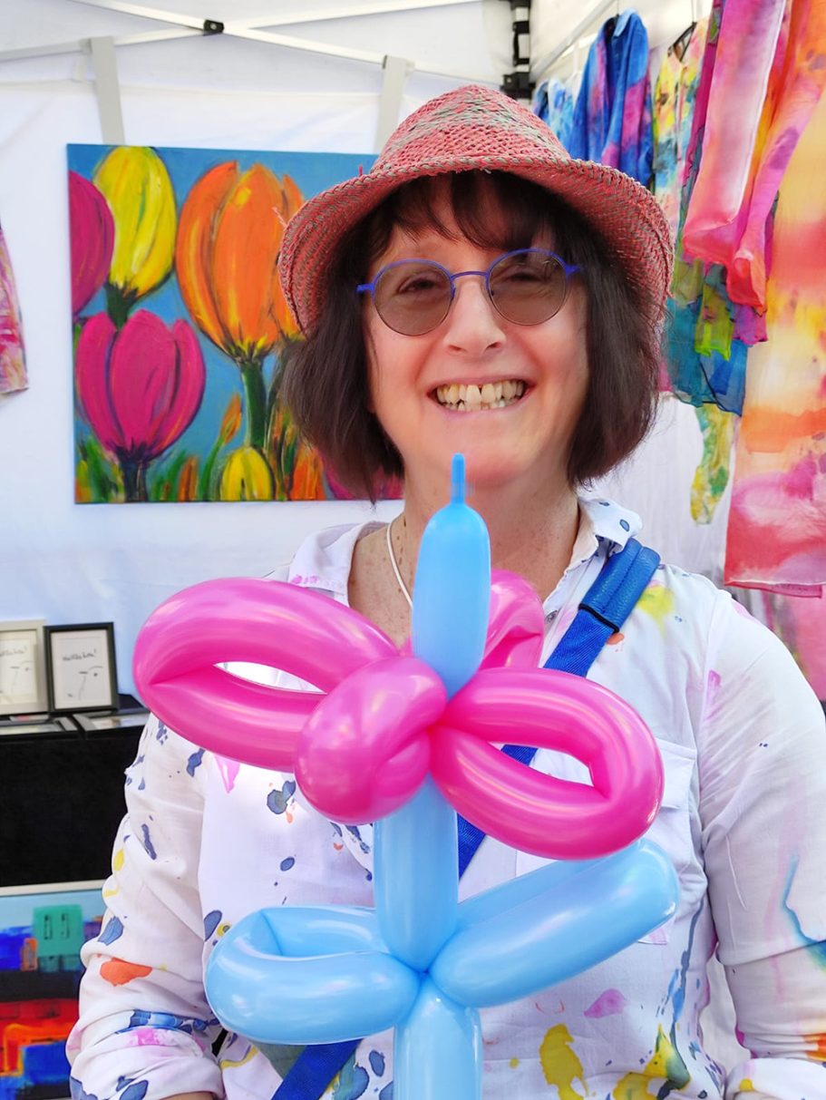 Frau mit Hut hält eine blau-pinke Ballonblume auf einem Kunsthandwerksmarkt.