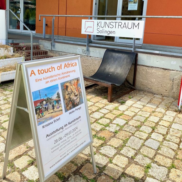 Informationstafel über die Veranstaltung "A touch of Africa" vor einem Gebäude.